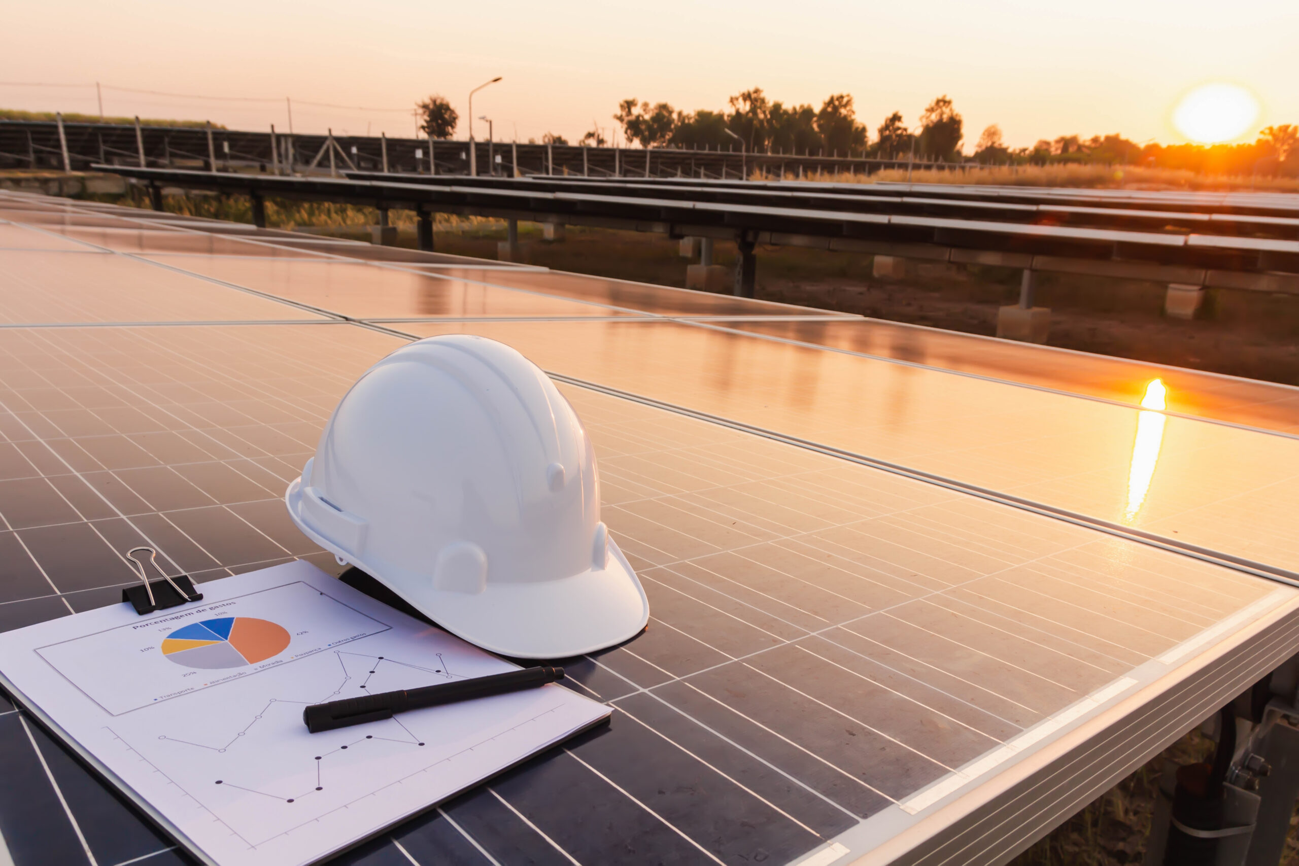 Schutzhelm und Projektplan auf Solarmodulen bei Sonnenuntergang
